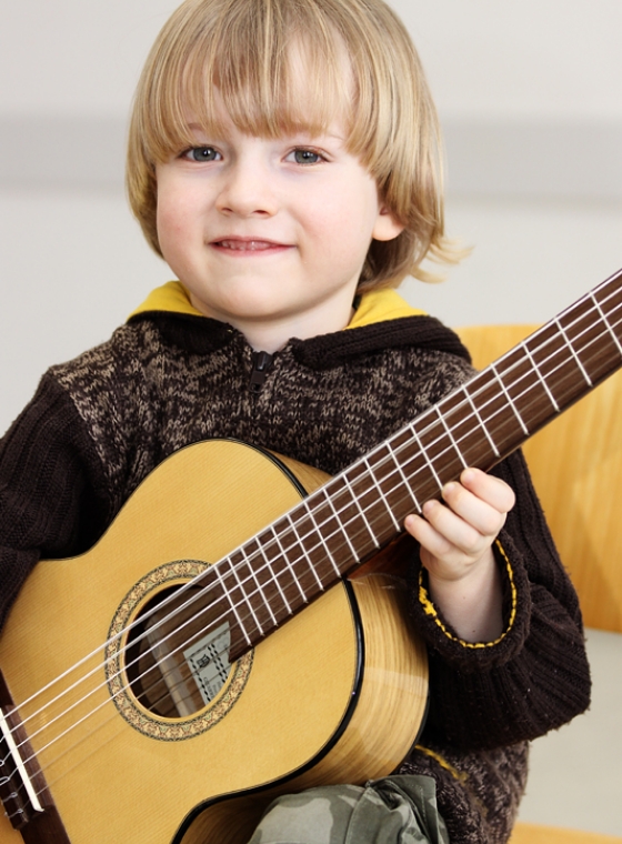 twin Werbeagentur | Business- und Imagefotografie | kleiner Junge sitzt zufrieden mit seiner Gitarre auf dem Stuhl