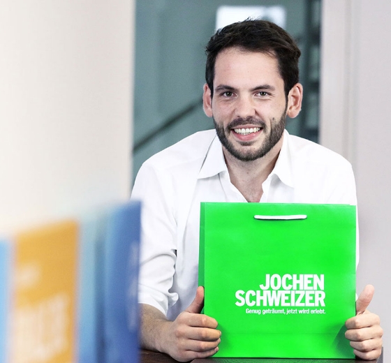twin Werbeagentur | Business- und Imagefotografie | junger Mann hält eine knallgrüne Tüte in der Hand mit dem Logo von Jochen Schweizer
